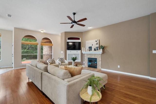 living area featuring a tiled fireplace, ceiling fan, wood finished floors, and baseboards