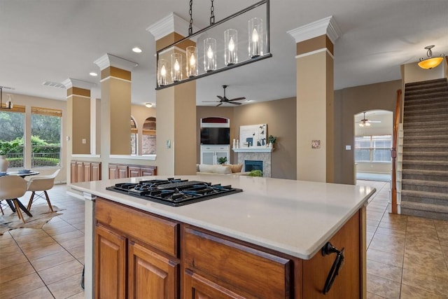kitchen featuring ceiling fan, black gas stovetop, light tile patterned floors, a glass covered fireplace, and light countertops