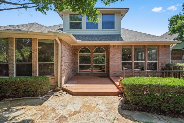 doorway to property featuring brick siding, a shingled roof, and a wooden deck