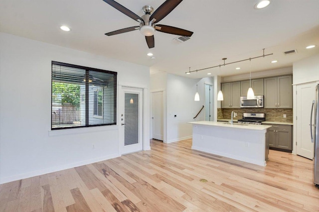 kitchen with stainless steel appliances, gray cabinetry, a ceiling fan, decorative backsplash, and light countertops