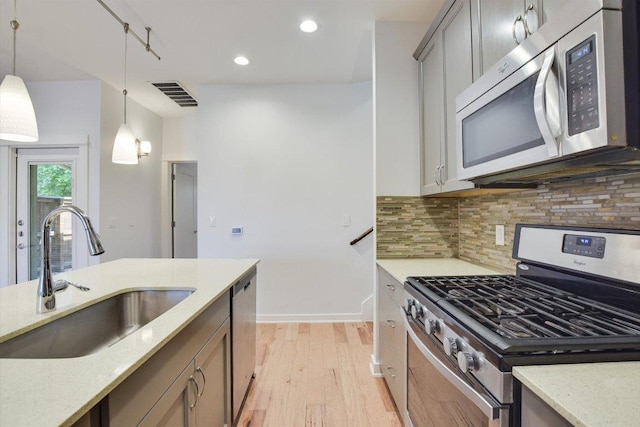 kitchen with stainless steel appliances, a sink, light wood finished floors, pendant lighting, and tasteful backsplash