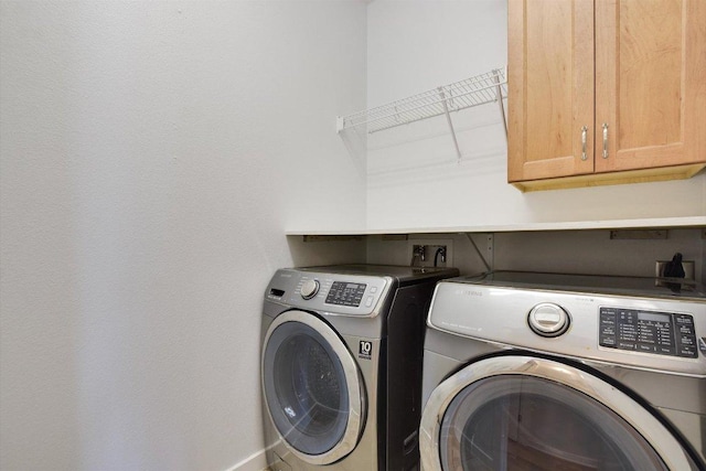 clothes washing area with washing machine and dryer, cabinet space, and baseboards