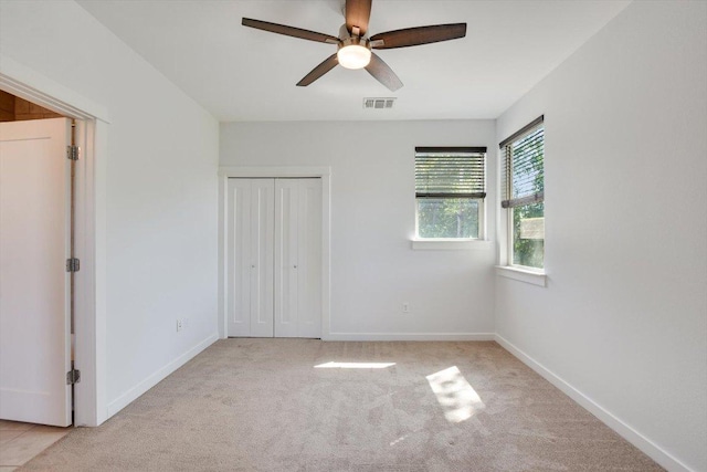 unfurnished bedroom featuring light carpet, a closet, baseboards, and a ceiling fan