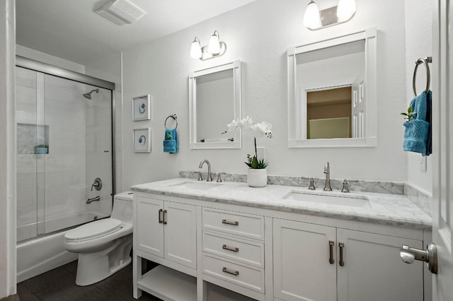 bathroom featuring toilet, double vanity, and bath / shower combo with glass door