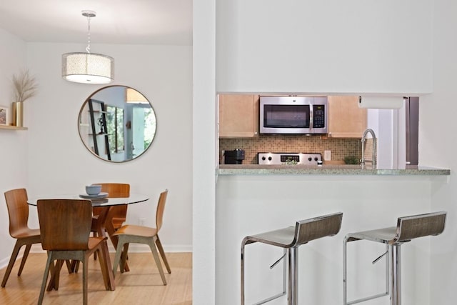 3204 Menchaca Rd Unit 716, Austin, TX 78704 - kitchen with stainless steel microwave, light wood-style floors, decorative backsplash, stove, and a breakfast bar