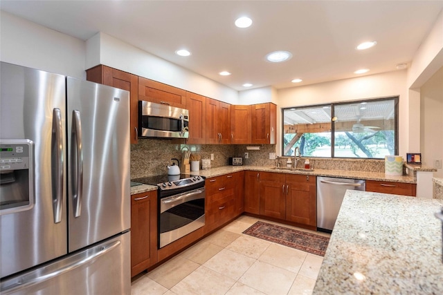 kitchen with appliances with stainless steel finishes, a sink, brown cabinetry, backsplash, and recessed lighting