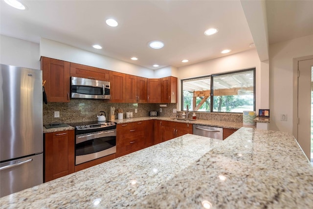 kitchen with appliances with stainless steel finishes, a sink, brown cabinets, light stone countertops, and recessed lighting