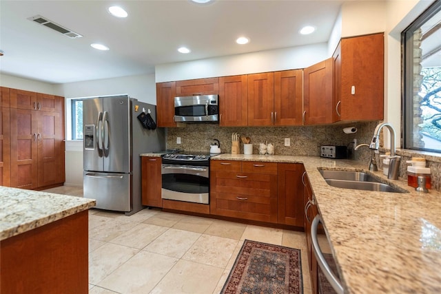 kitchen with stainless steel appliances, a sink, backsplash, light stone counters, and light tile patterned floors