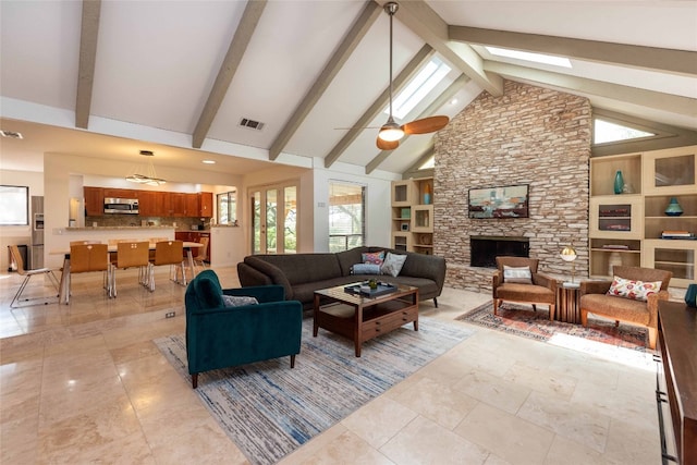living room with high vaulted ceiling, beam ceiling, a fireplace, a ceiling fan, and a skylight
