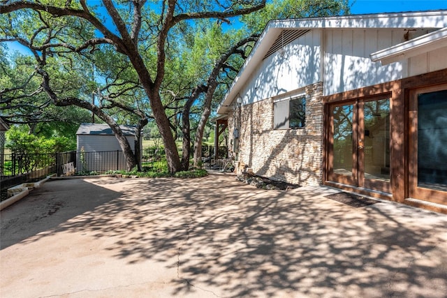 view of patio with a storage unit, an outbuilding, fence, and french doors