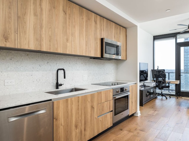 kitchen with stainless steel appliances, modern cabinets, a sink, light wood finished floors, and decorative backsplash