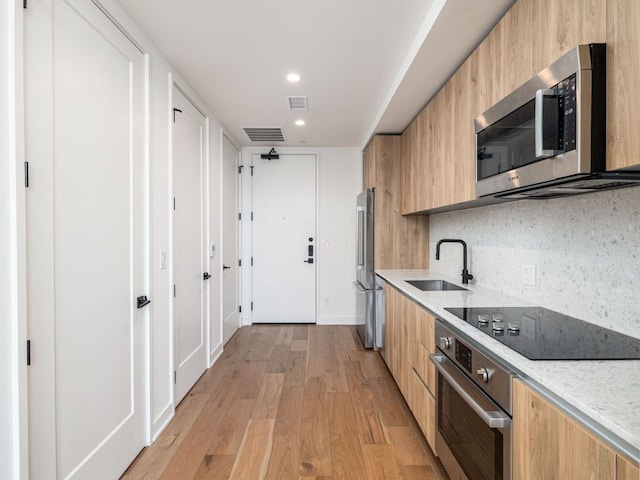 kitchen with stainless steel appliances, a sink, modern cabinets, light wood-style floors, and decorative backsplash