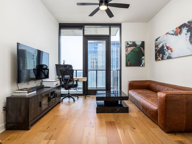 living area featuring expansive windows, an office area, light wood-style floors, and a ceiling fan