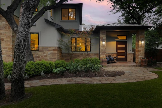 401 Rocky River Rd, West Lake Hills, TX 78746 - back of property at dusk with stone siding, stucco siding, a standing seam roof, a yard, and metal roof