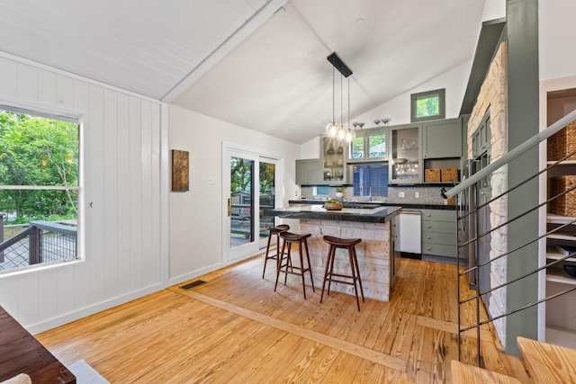 kitchen with green cabinetry, dark countertops, vaulted ceiling, light wood-style flooring, and a breakfast bar area
