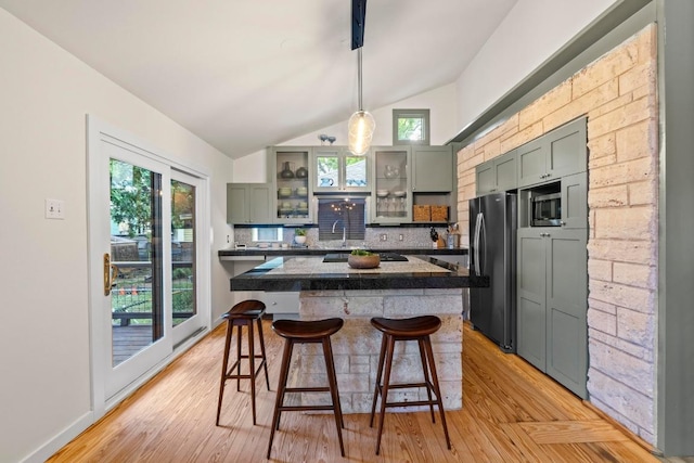 kitchen featuring freestanding refrigerator, lofted ceiling, a kitchen breakfast bar, backsplash, and light wood-style flooring