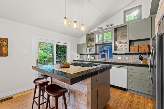 kitchen with white dishwasher, black stovetop, freestanding refrigerator, a breakfast bar area, and lofted ceiling