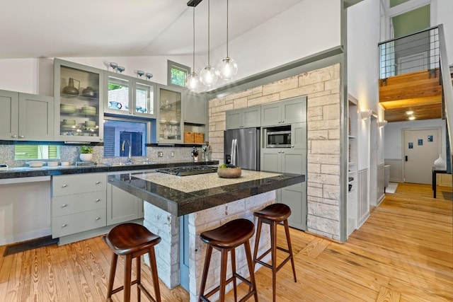 kitchen with stainless steel appliances, a kitchen breakfast bar, light wood finished floors, a sink, and high vaulted ceiling
