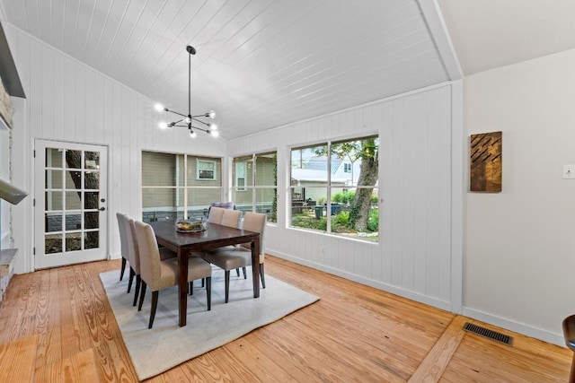 dining area featuring baseboards, light wood-style flooring, a chandelier, wooden walls, and lofted ceiling
