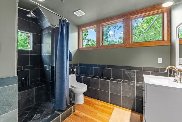 bathroom with tile walls, a tile shower, wood finished floors, toilet, and vanity
