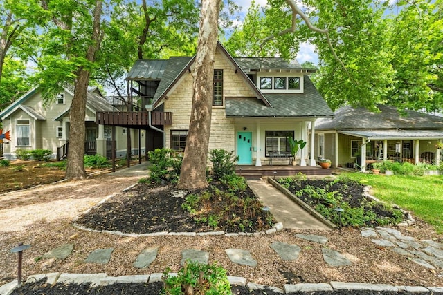 tudor house with a porch, a shingled roof, and stone siding