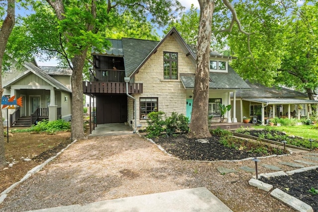 view of front of house featuring stone siding, a porch, driveway, a shingled roof, and a balcony