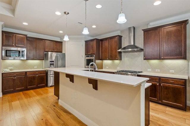 419 Davis Mountain Cir, Georgetown, TX 78633 - kitchen featuring stainless steel appliances, wall chimney exhaust hood, ornamental molding, a kitchen island with sink, and light wood-style floors