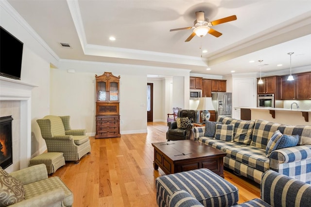 419 Davis Mountain Cir, Georgetown, TX 78633 - living room featuring a tray ceiling, a ceiling fan, light wood finished floors, a tile fireplace, and ornamental molding