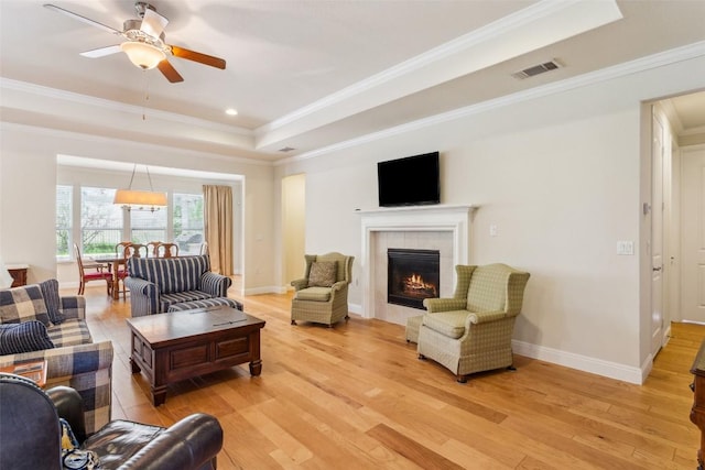 419 Davis Mountain Cir, Georgetown, TX 78633 - living room featuring a tray ceiling, light wood-style flooring, crown molding, a tile fireplace, and ceiling fan