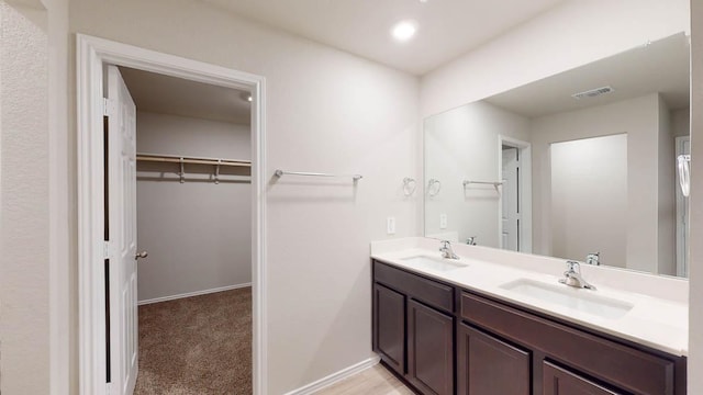 full bath featuring a walk in closet, double vanity, baseboards, and recessed lighting