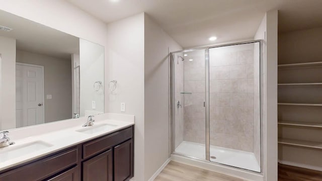 full bathroom with a shower stall, wood finished floors, double vanity, and recessed lighting