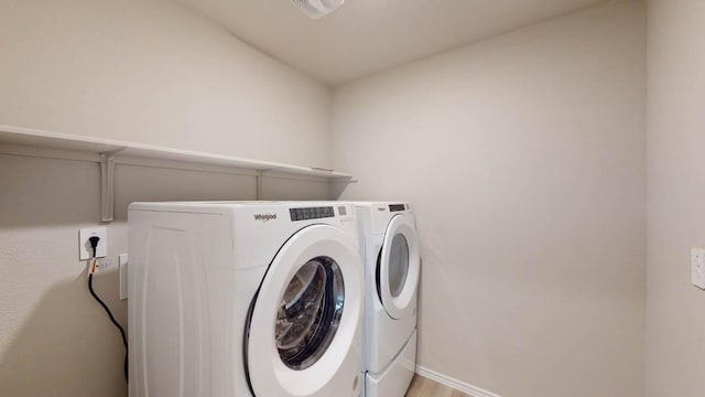 clothes washing area featuring washing machine and clothes dryer, baseboards, and light wood-type flooring