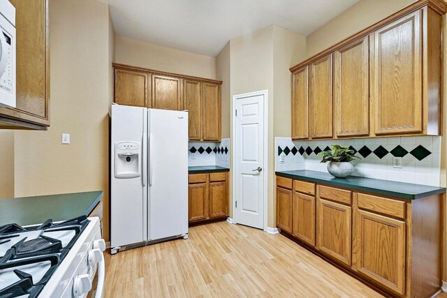 2713 Oakwood Glen Dr, Cedar Park, TX 78613 - kitchen with white appliances, dark countertops, light wood-style floors, brown cabinetry, and tasteful backsplash