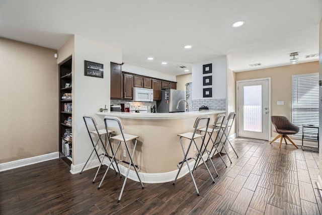 6900 E Riverside Dr Unit 6, Austin, TX 78741 - kitchen featuring white microwave, freestanding refrigerator, dark wood-style floors, backsplash, and a kitchen breakfast bar