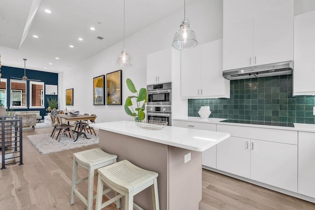 kitchen with under cabinet range hood, double oven, light wood-style floors, light countertops, and tasteful backsplash