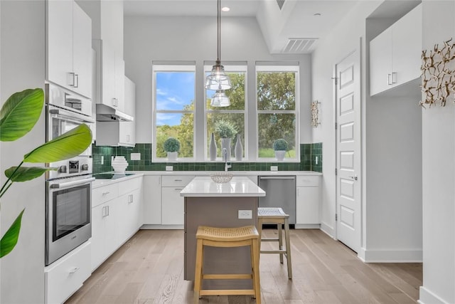 kitchen featuring dishwasher, black electric cooktop, tasteful backsplash, light wood finished floors, and lofted ceiling
