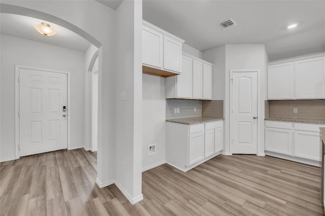 kitchen with arched walkways, light wood-style floors, decorative backsplash, white cabinets, and recessed lighting