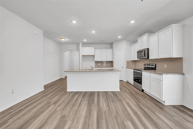 kitchen featuring appliances with stainless steel finishes, recessed lighting, light wood-type flooring, decorative backsplash, and arched walkways
