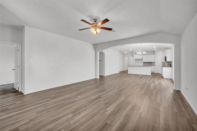 unfurnished living room featuring arched walkways, ceiling fan, a chandelier, wood finished floors, and baseboards