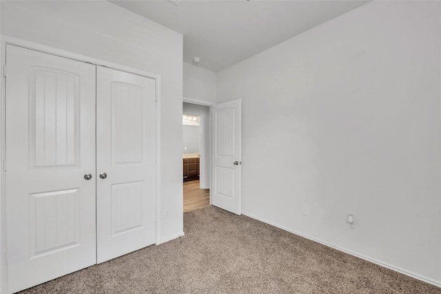 unfurnished bedroom with light carpet, a closet, and baseboards