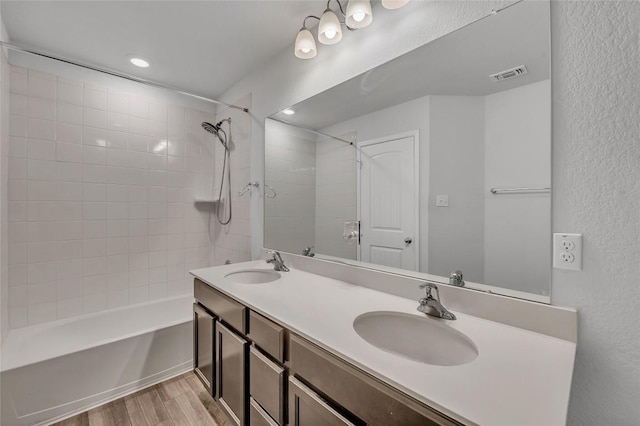 full bath with wood finished floors, tub / shower combination, a textured wall, double vanity, and recessed lighting