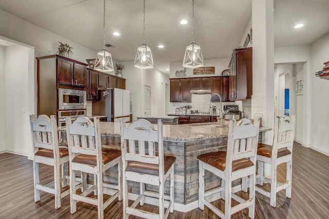 kitchen with stainless steel appliances, decorative backsplash, light stone counters, wood finished floors, and dark brown cabinets