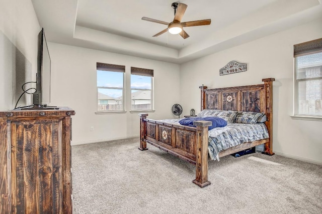 bedroom featuring carpet flooring, a tray ceiling, baseboards, and ceiling fan