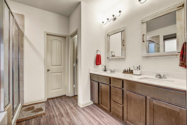 bathroom featuring a stall shower, wood finished floors, double vanity, and baseboards