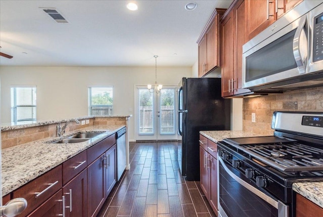 kitchen featuring appliances with stainless steel finishes, a sink, backsplash, light stone counters, and dark wood-style flooring