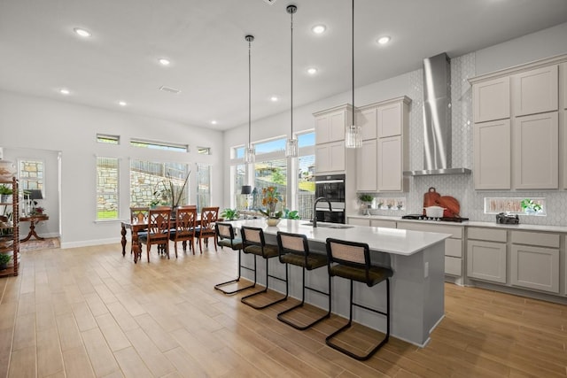 147 Epoch Dr, Austin, TX 78737 - kitchen with wall chimney range hood, light countertops, a kitchen breakfast bar, an island with sink, and tasteful backsplash