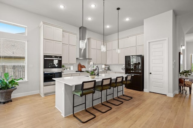 147 Epoch Dr, Austin, TX 78737 - kitchen with freestanding refrigerator, wall chimney range hood, stainless steel double oven, light countertops, and a breakfast bar area