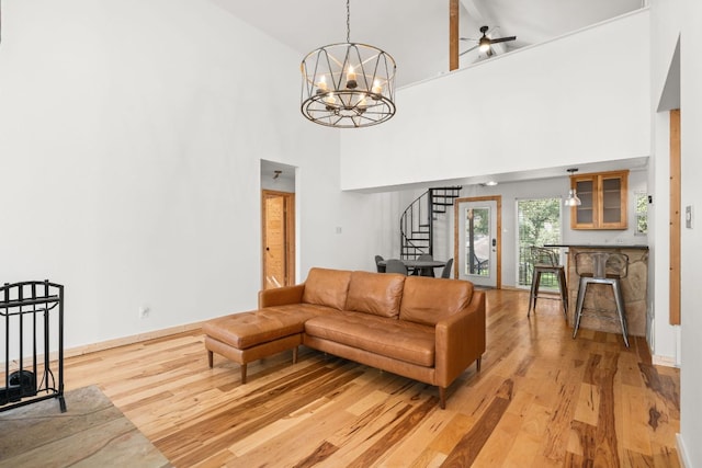 living room featuring stairs, light wood-style floors, a towering ceiling, a chandelier, and a ceiling fan