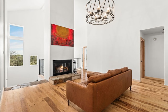 living area featuring a towering ceiling, light wood-type flooring, a glass covered fireplace, a chandelier, and baseboards
