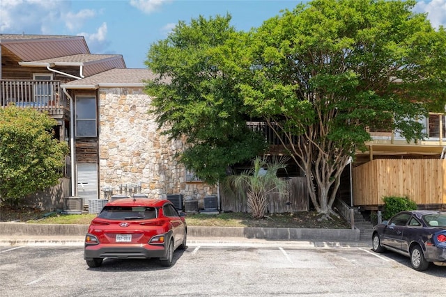 view of front of house featuring stone siding, uncovered parking, a shingled roof, and central air condition unit